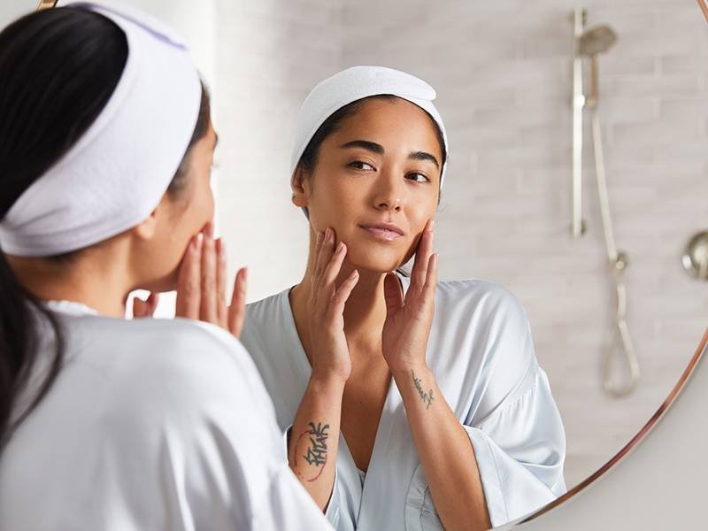 Image of woman wearing a white bathrobe and looking at her face in the mirror